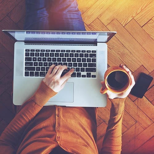 Laptop and coffee cup in girls hands sitting on a wooden floor