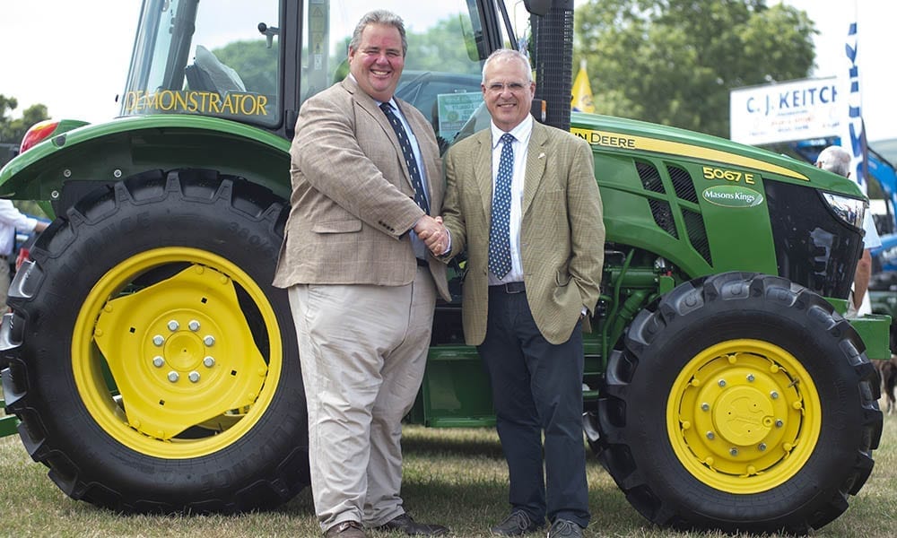 two men shaking hands in front of tractor